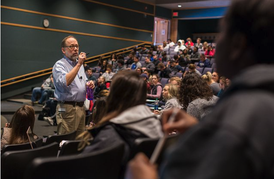 An image of a professor is shown lecturing to a room of students at Indiana University.
